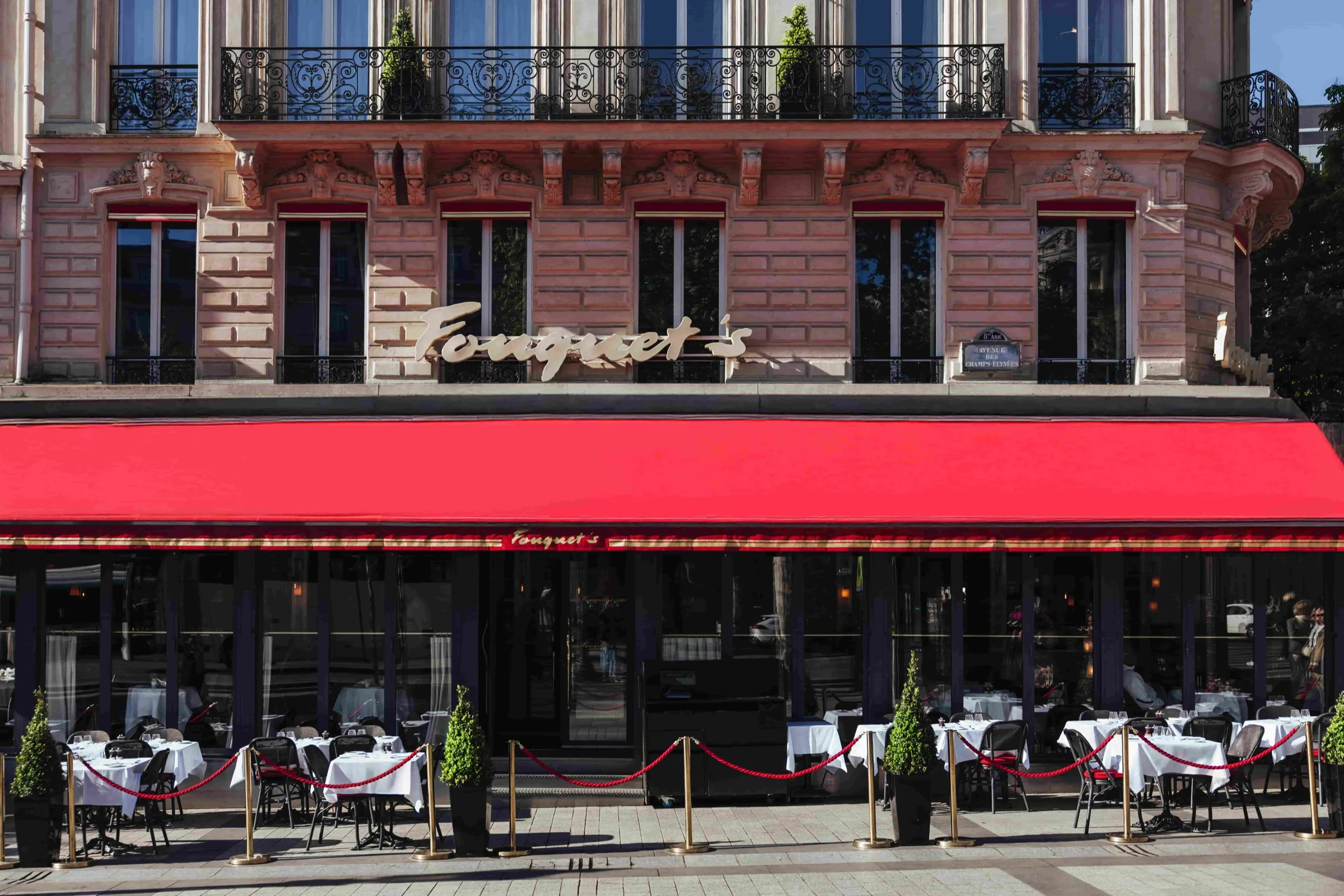 Fouquet’s Paris’s ground-floor facade on the Champs-Élysées, gold signage above a red awning and pavement terrace.