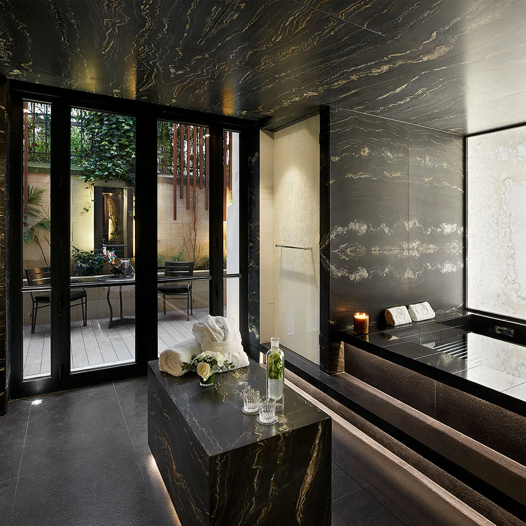 A dark-stone spa treatment room opening onto a private planted courtyard.