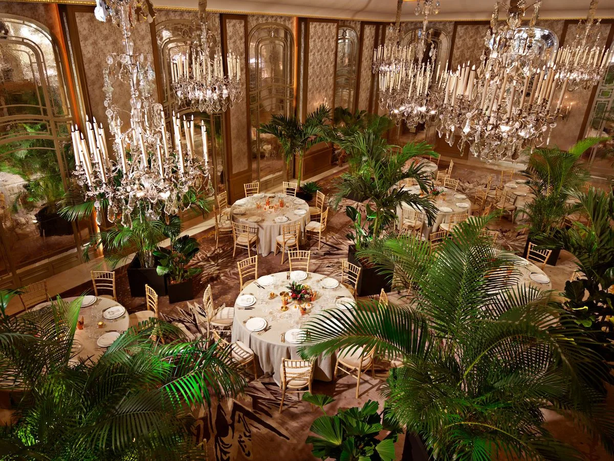 An elegant salon at Hôtel Plaza Athénée set for a private event, crystal chandeliers above round tables and palms.