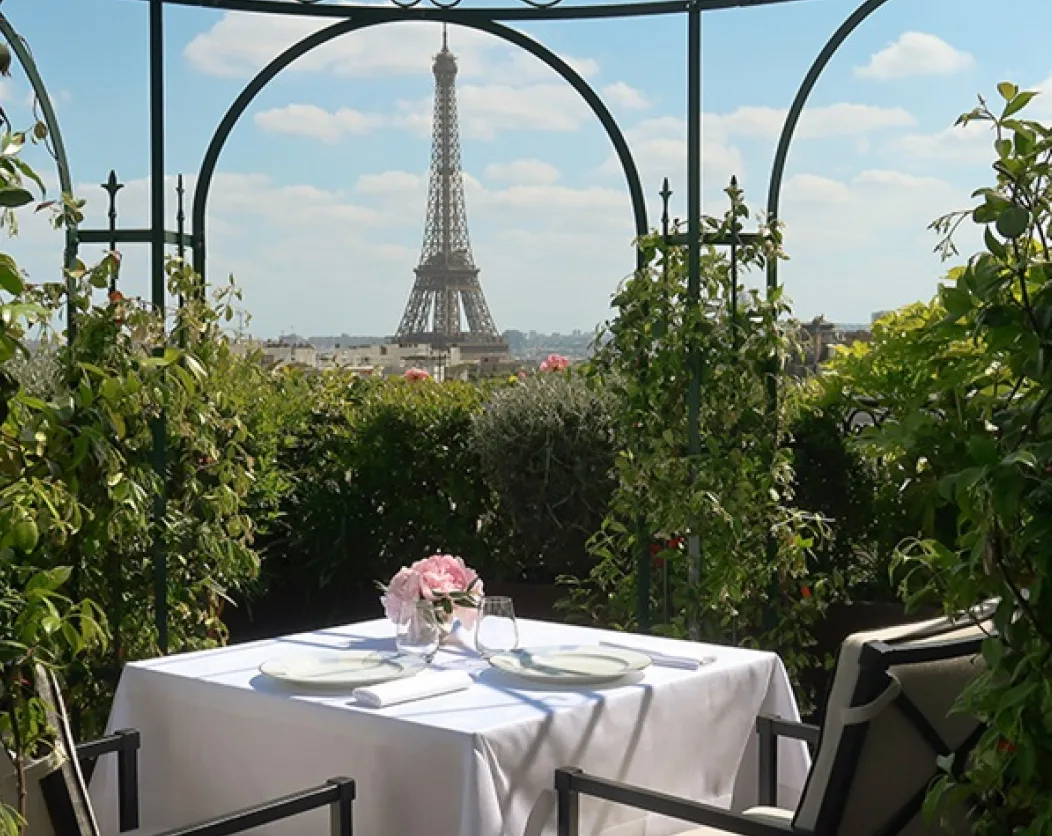 Une table dressée sur la terrasse-jardin de L'Oiseau Blanc, encadrée par une pergola en fer, avec la tour Eiffel en toile de fond.