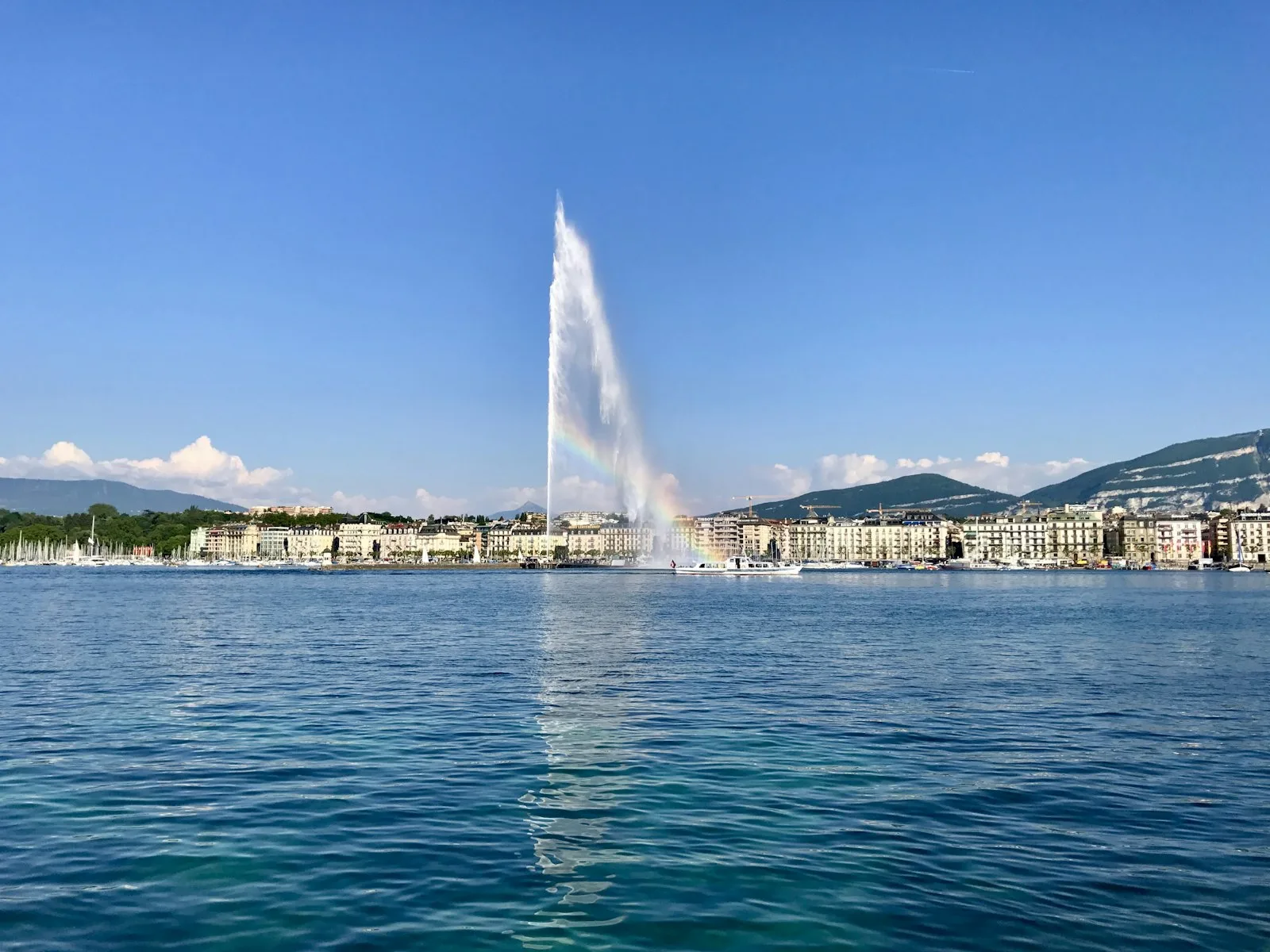 Le Jet d'Eau sur le lac Léman, avec un arc-en-ciel et la silhouette de la ville en arrière-plan.