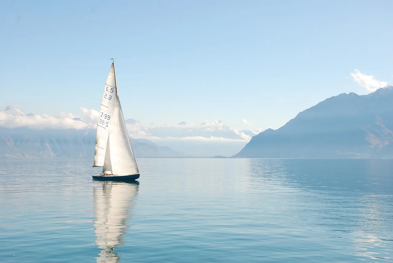 Un voilier seul sur les eaux calmes du lac Léman, avec les Alpes à l'horizon.