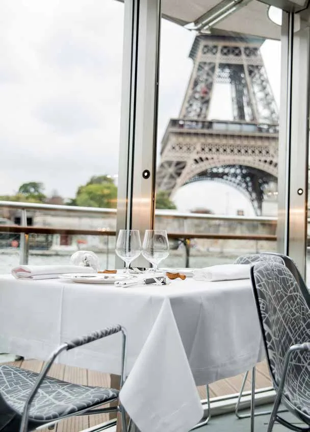A table set for two aboard Ducasse sur Seine, the Eiffel Tower framed through the window.