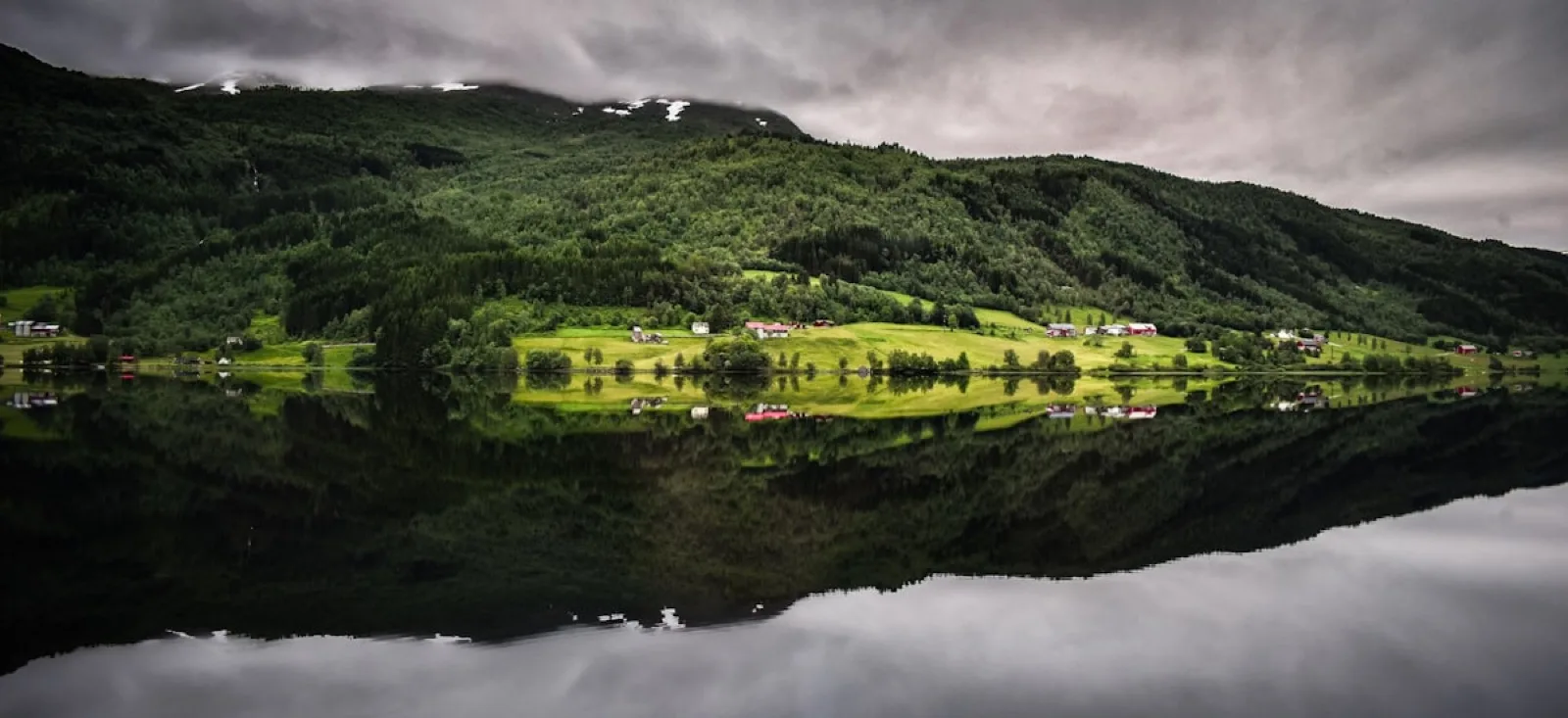 Un village norvégien niché dans un fjord, reflété dans une eau calme sous des montagnes verdoyantes.