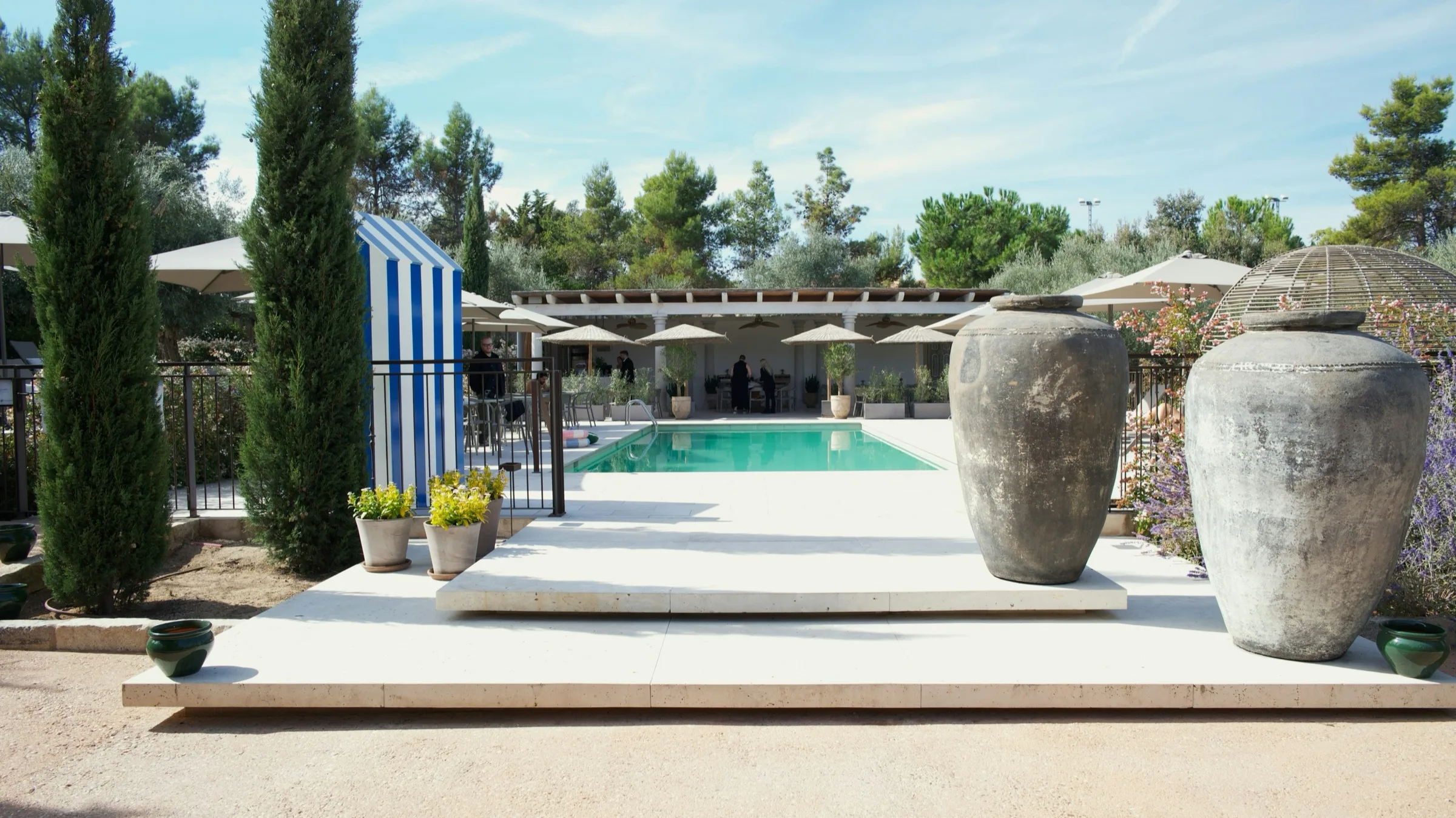 La terrasse d’une piscine de villa privée en Provence, entre cyprès et jarres en terre cuite.