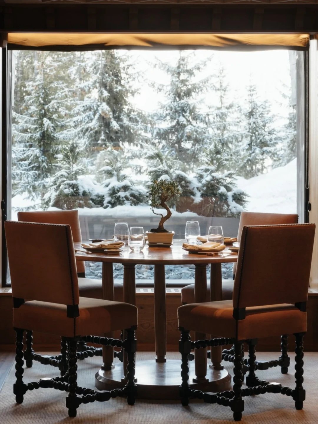 一张摆好餐具的餐桌,落地窗外是积雪的松林。