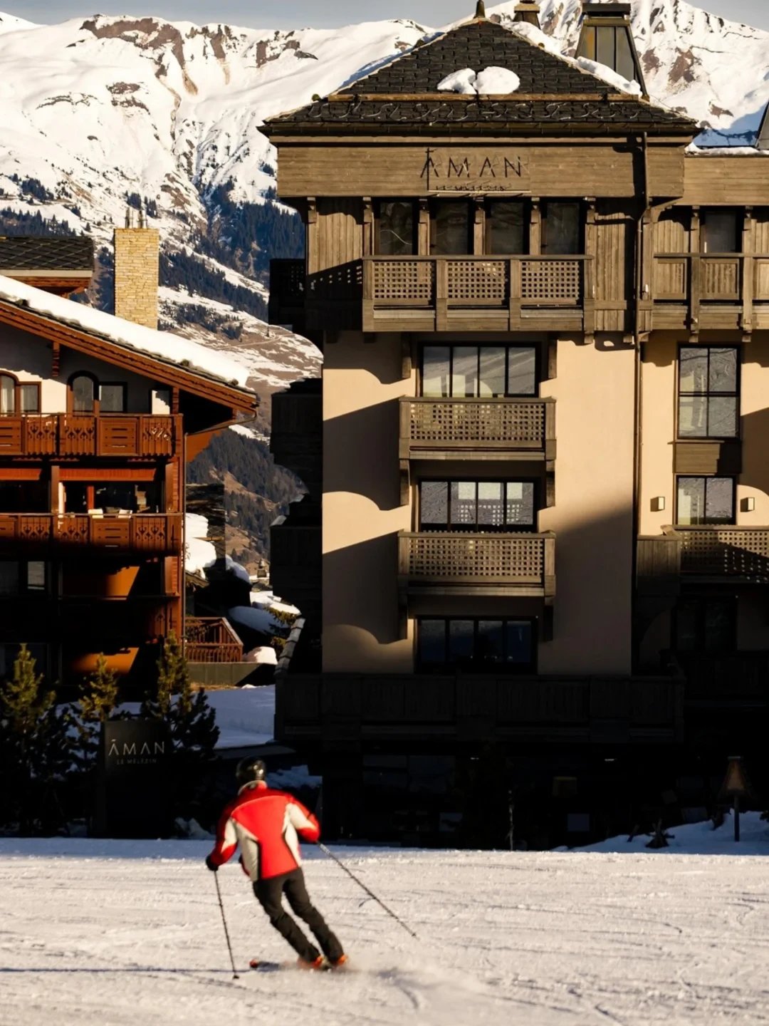 A skier heading toward the Aman Le Mélézin chalet, its signage visible against the mountains.