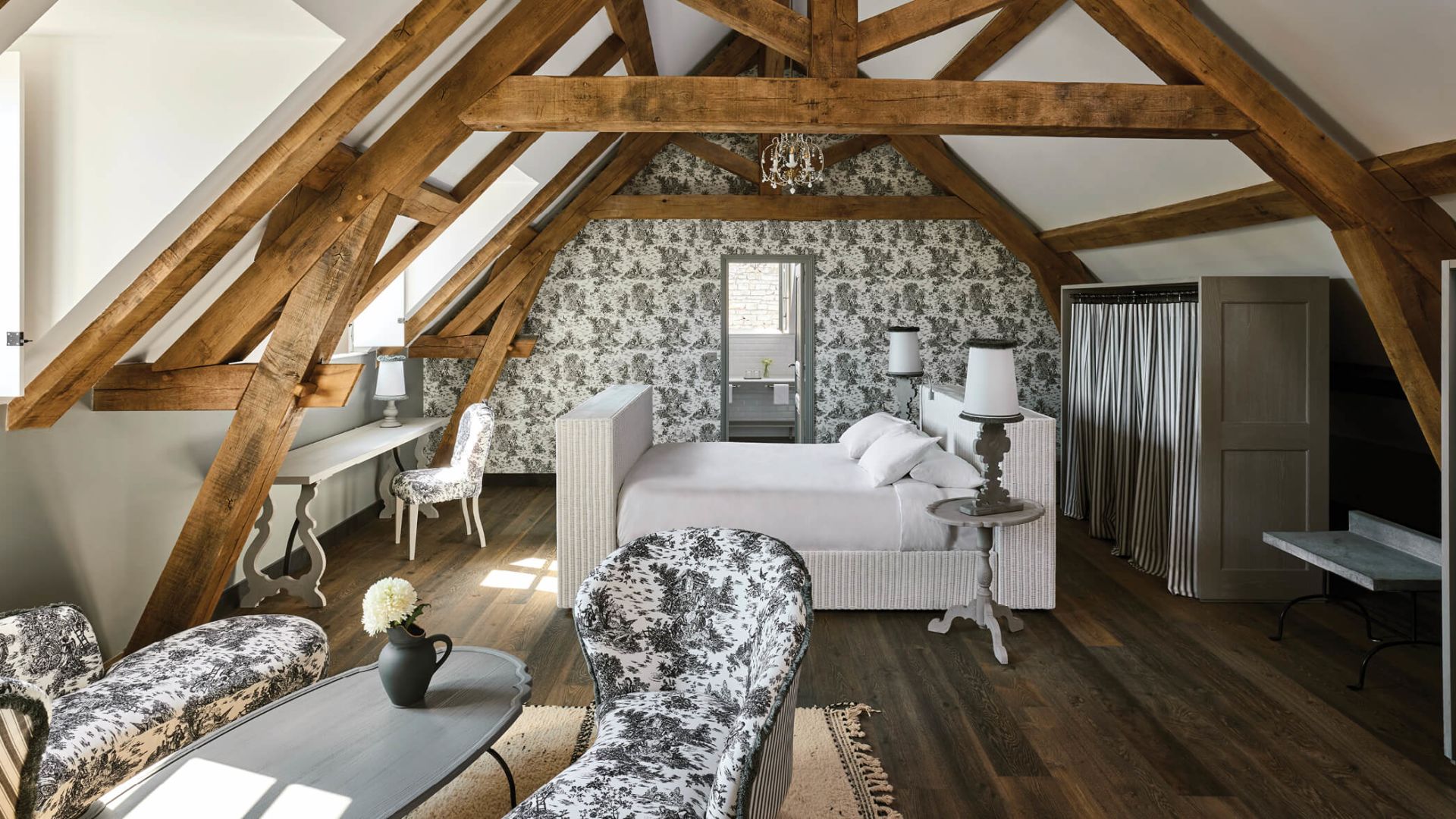 The Montrachet Suite's bedroom, papered in toile de Jouy beneath the original roof timbers.