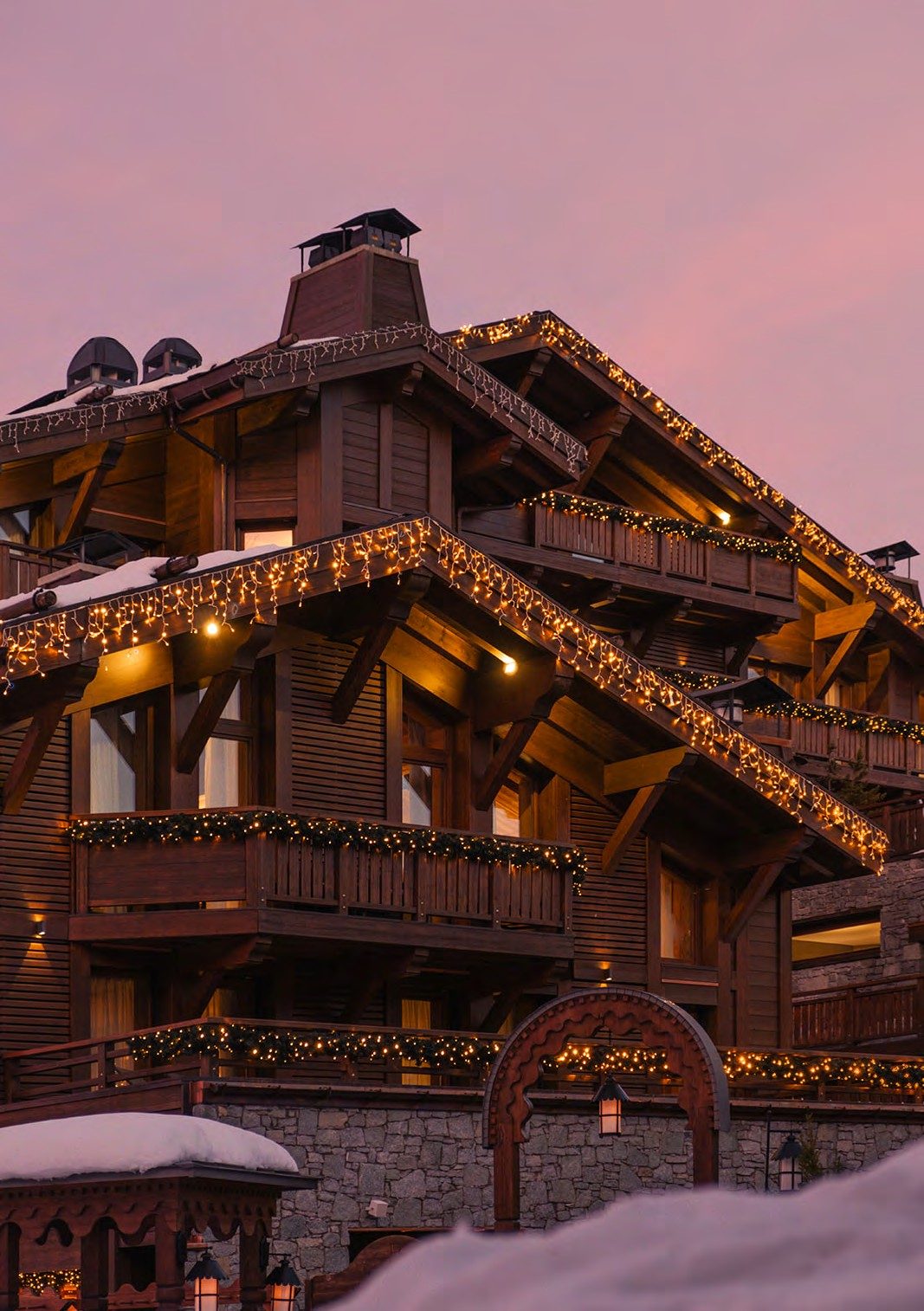 黄昏时分的 Fouquet’s Courchevel，木屋外墙上暖黄色的灯饰映衬着粉紫色天空