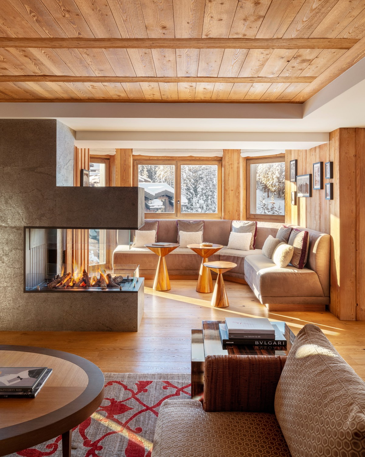 Fouquet’s Courchevel suite living room, a three-sided open fire beside a timber-panelled seating area