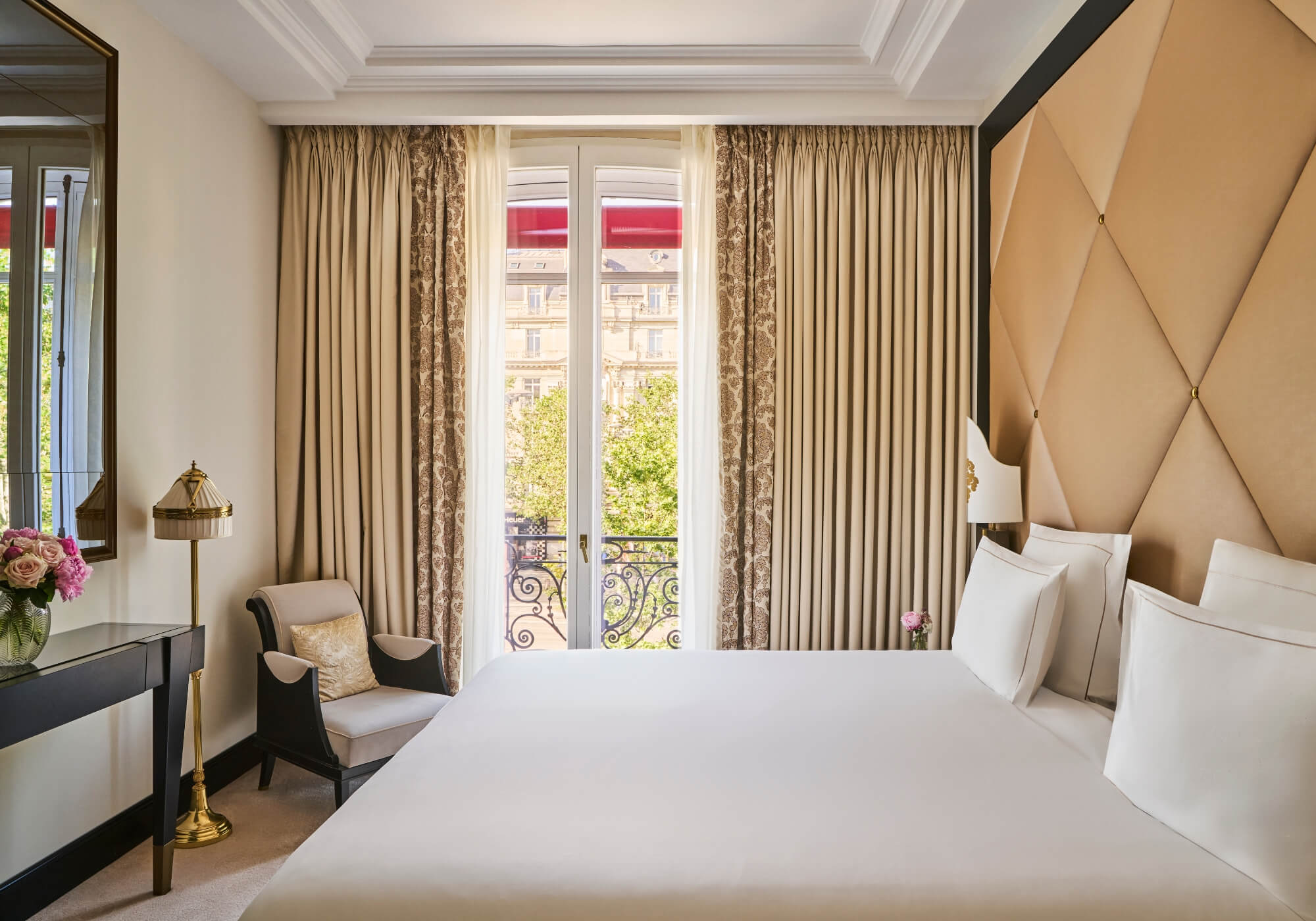 Fouquet’s Paris Champs-Élysées Prestige Suite, a gold quilted headboard beside French doors opening onto a wrought-iron balcony