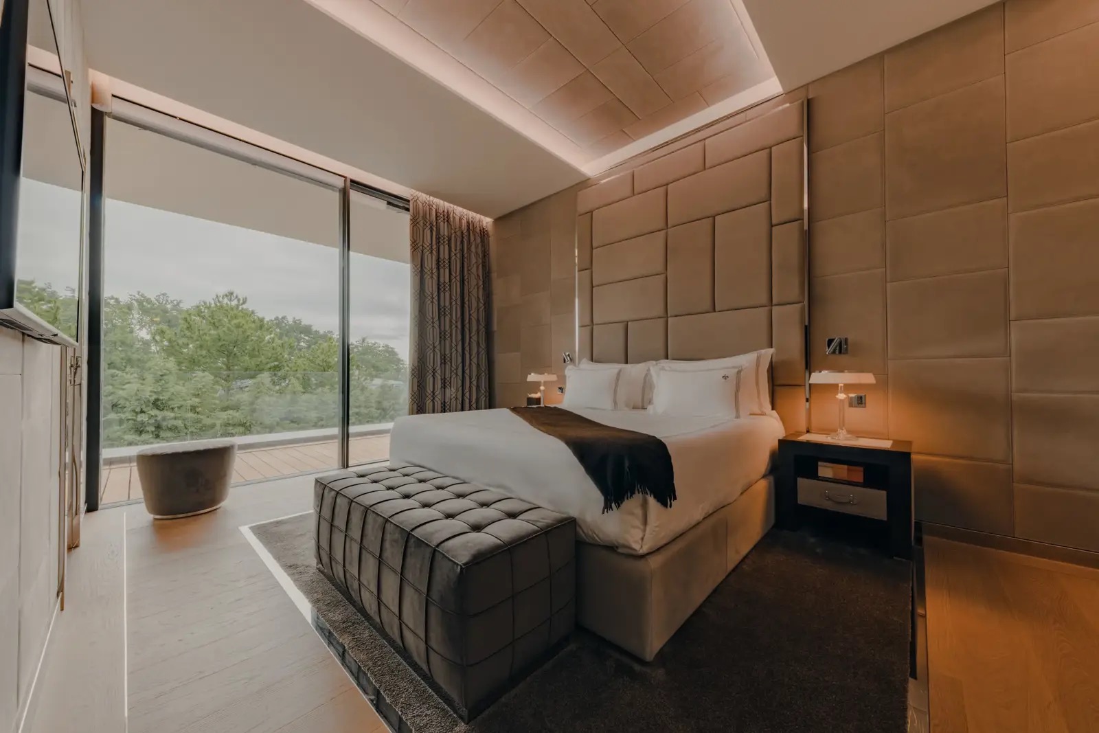 A bedroom with a floor-to-ceiling glass wall opening onto a private terrace.