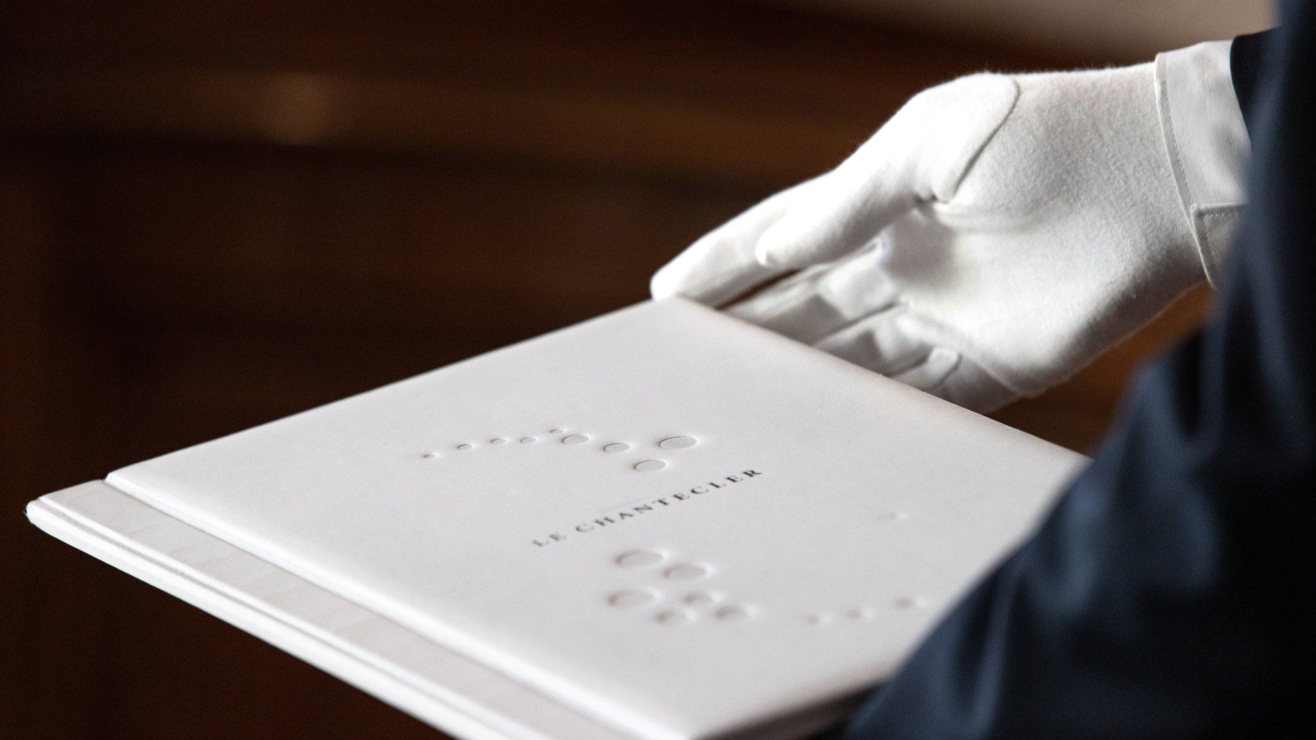 A white-gloved server presents the menu at Le Chantecler, embossed in Braille.