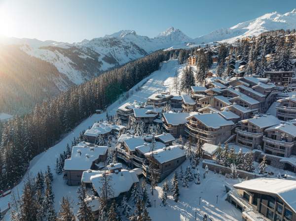 A daytime aerial view of Le K2 Palace’s chalets spread across the hillside among the pines.