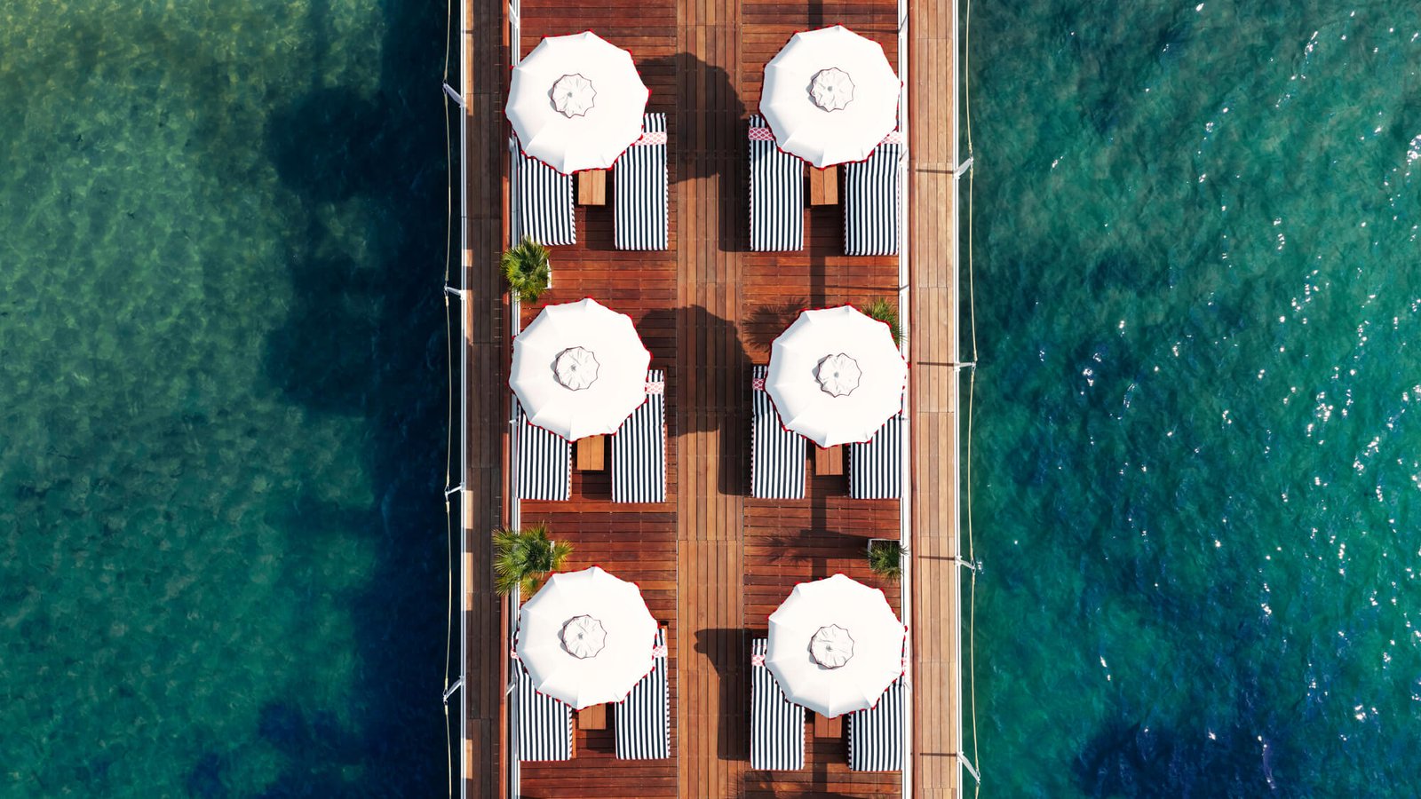 Vue aérienne du ponton de la plage privée du Majestic, transats rayés sur une mer turquoise.