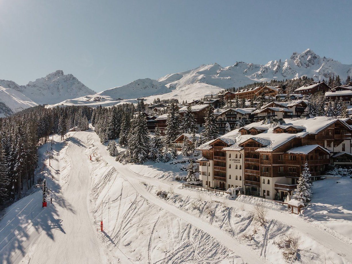 Hôtel Le Strato 紧邻雪道而建，积雪覆盖的木屋外墙上可见招牌