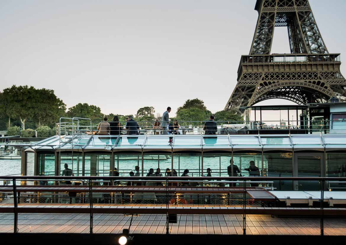 Des convives sur le pont supérieur de Ducasse sur Seine au crépuscule, la tour Eiffel en arrière-plan.