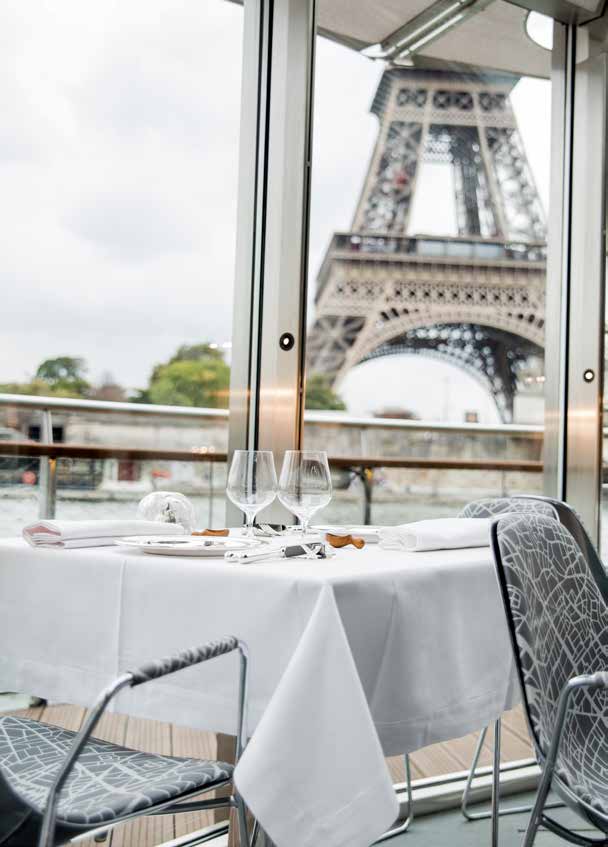 Une table dressée pour deux à bord de Ducasse sur Seine, la tour Eiffel encadrée par la fenêtre.