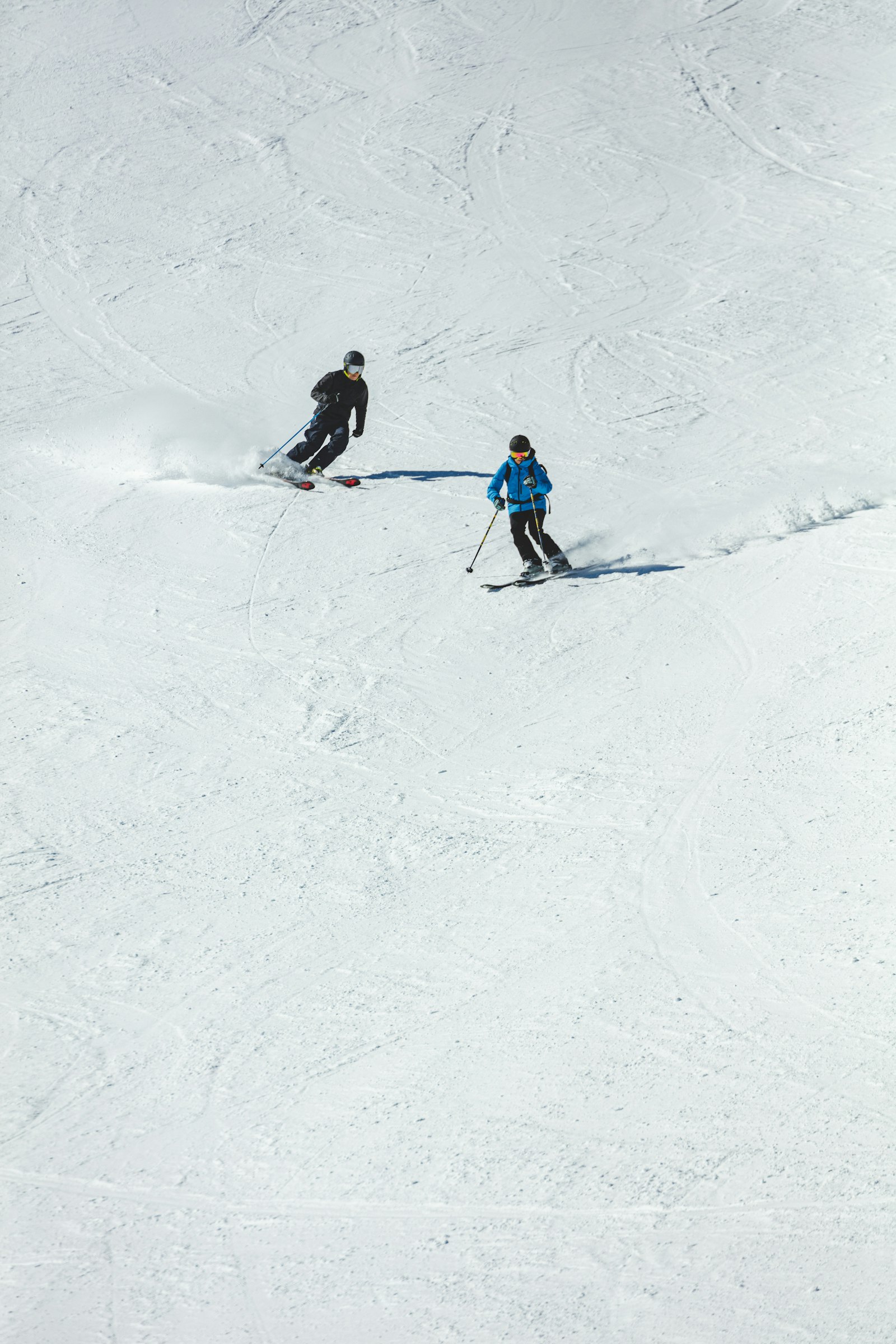 Two skiers carving fresh tracks down an open off-piste slope.