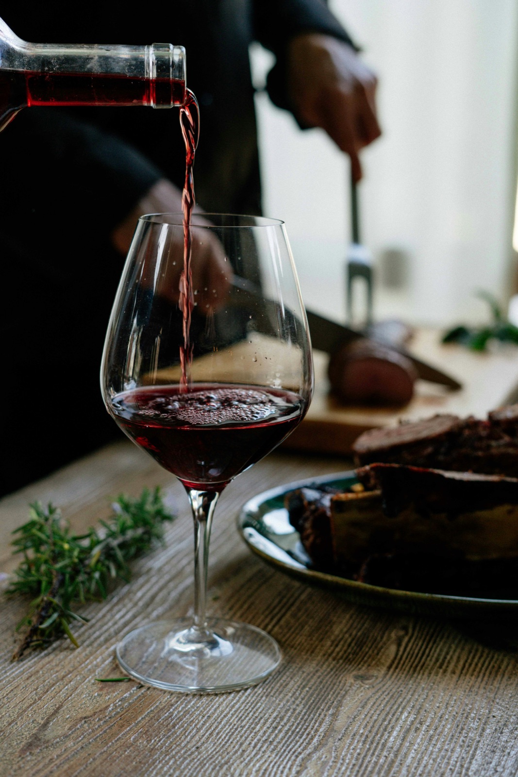 Red wine being poured into a glass, hands only, no faces visible.