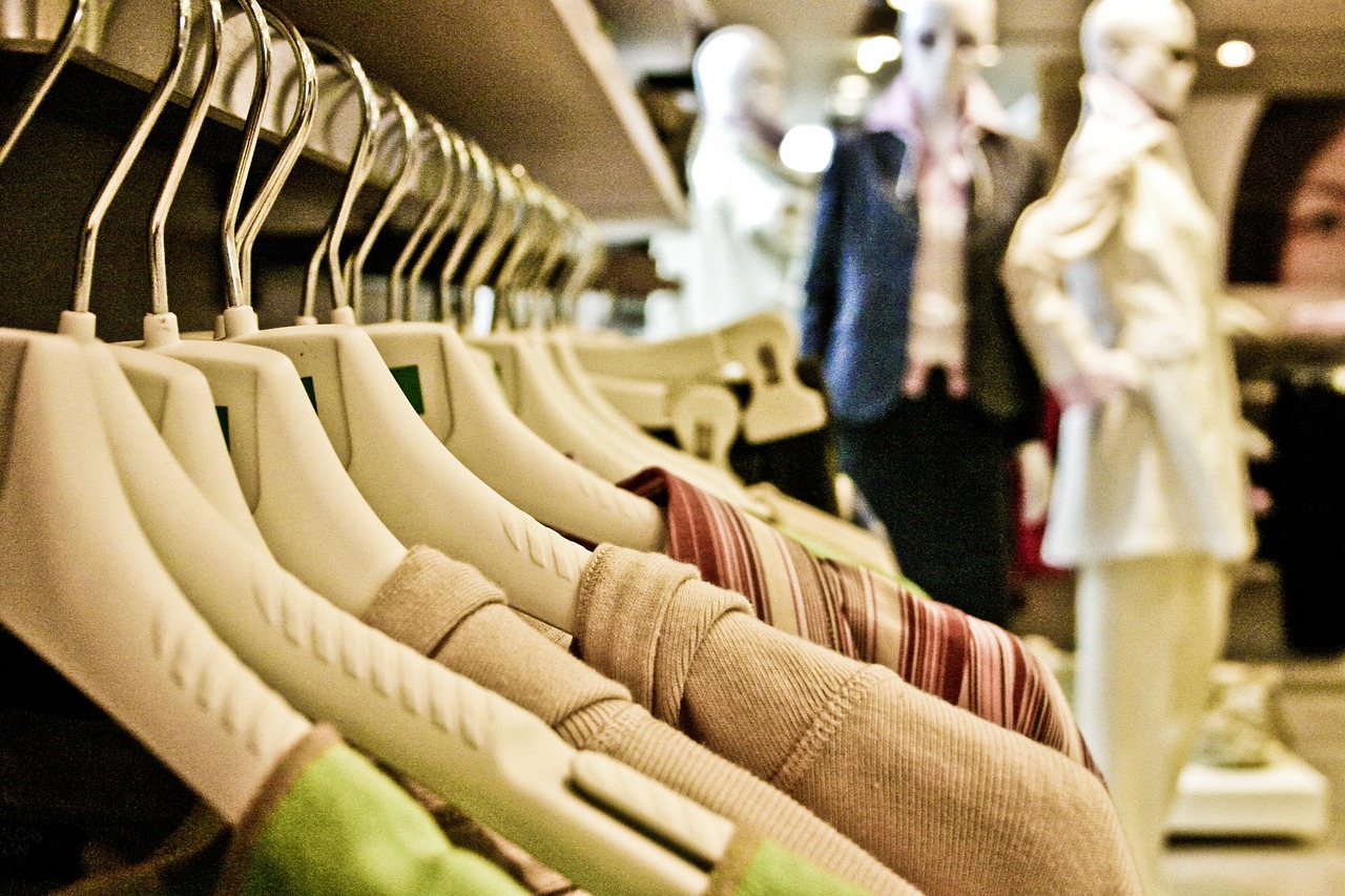 A rack of folded garments on hangers, with mannequins in soft focus behind.