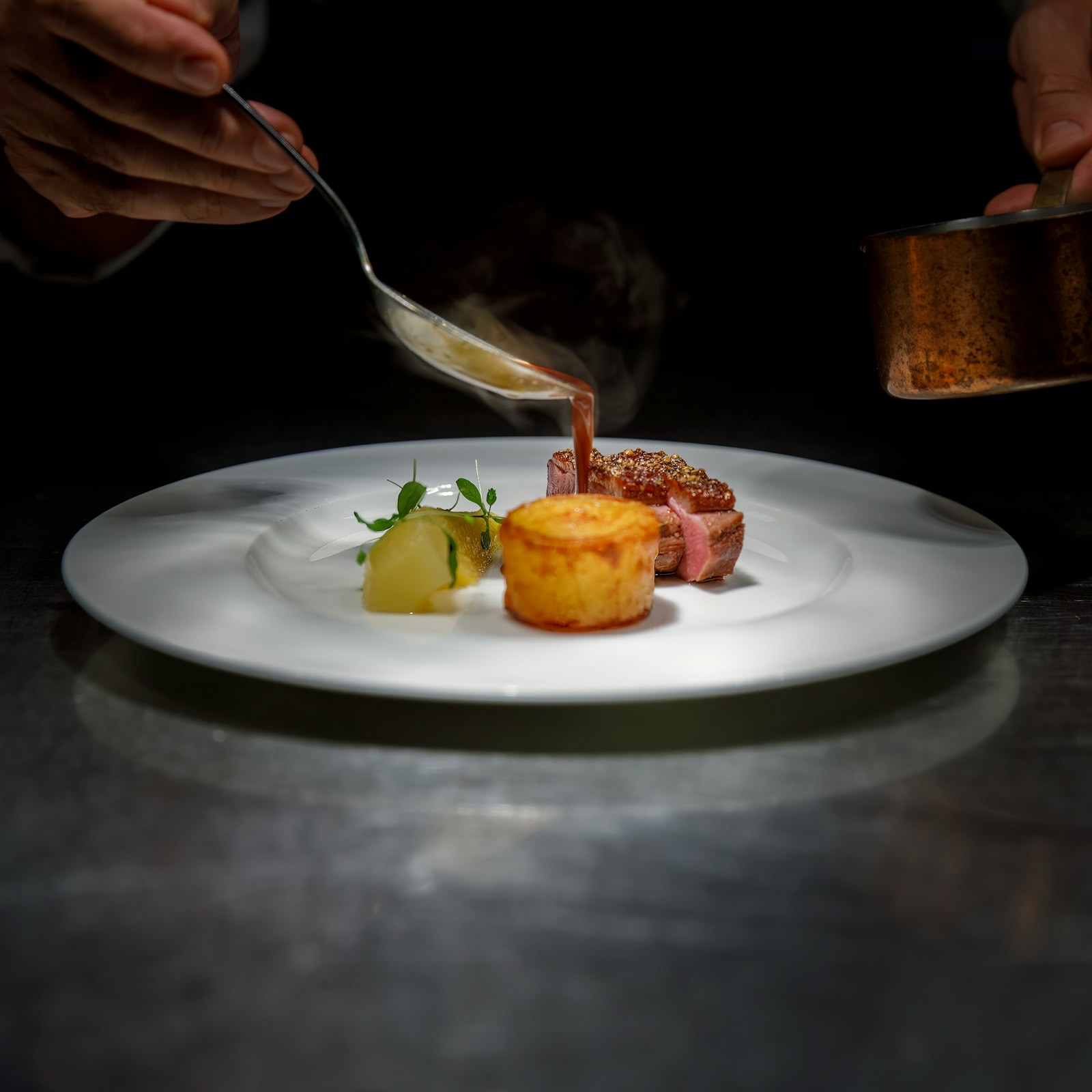 Les mains d’un chef finalisant un plat dressé avec une sauce.