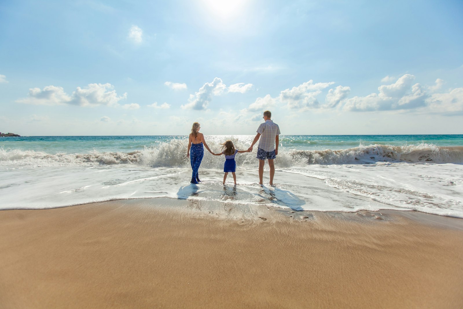 A family of three holding hands and walking along the seashore.