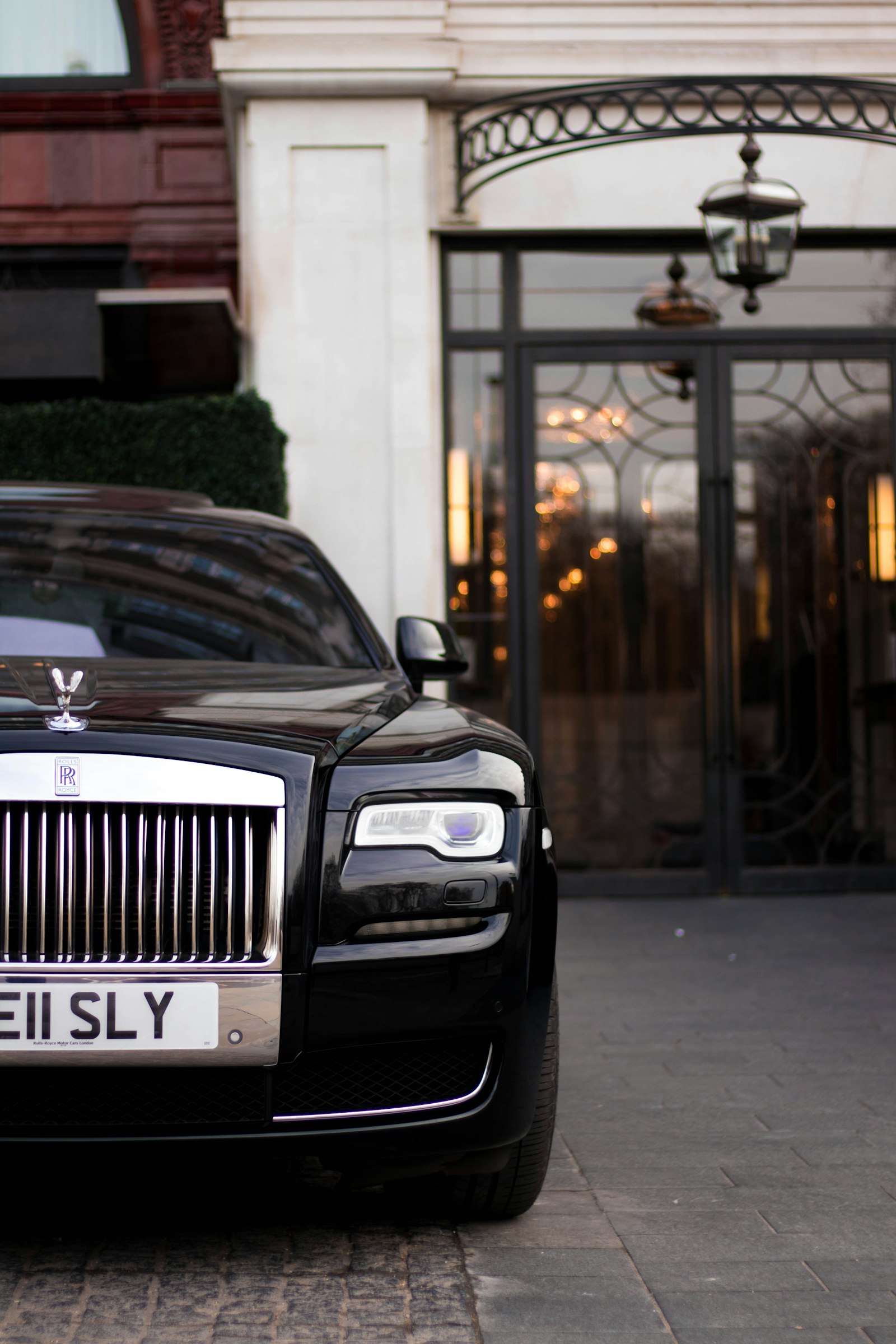 A black luxury chauffeured car parked outside an elegant hotel entrance.