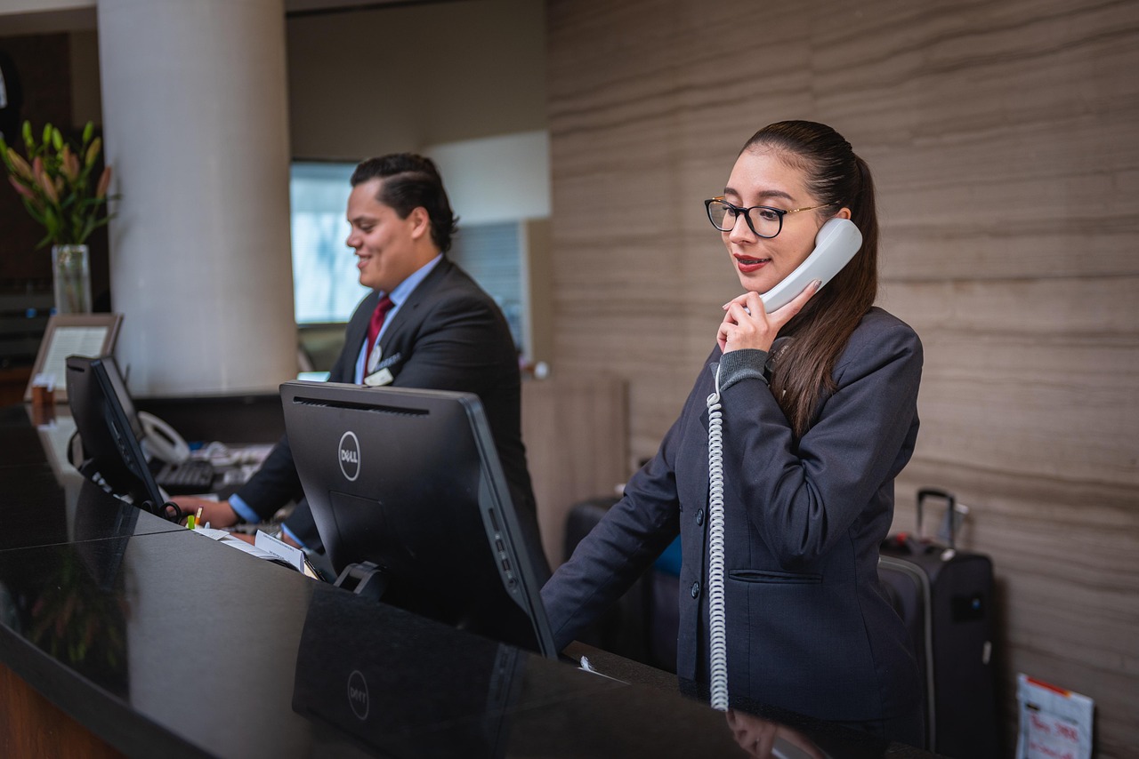 Une réceptionniste d'hôtel répondant au téléphone, avec la valise d'un client posée au comptoir.
