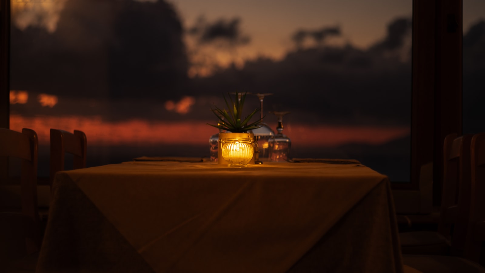 A candlelit table set for two on a terrace at sunset.